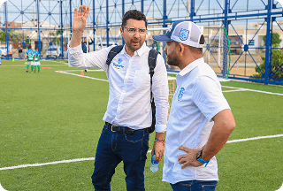 Dos integrantes del comité organizador conversando sobre una cancha de fútbol